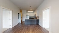 This thoughtfully designed single-floor residence showcases a clean, contemporary aesthetic with a neutral color palette and quality finishes throughout. The heart of the home is an open-concept kitchen that flows seamlessly into the living area, featuring a large peninsula with a light quartz countertop and dark wood-tone base, white upper cabinetry with matte black hardware, a tile backsplash, and a full suite of stainless steel appliances including a refrigerator, electric range, over-the-range microwave, and dishwasher. A sleek linear pendant light anchors the kitchen space. Wood-look plank flooring runs through the main living and kitchen areas, adding warmth and continuity. The bedrooms are carpeted and filled with natural light from large windows with exterior views, offering a calm and comfortable retreat. The primary bedroom benefits from notably high ceilings and direct access to both a walk-in closet — equipped with wire shelving systems — and a full en-suite bathroom featuring a sliding glass walk-in shower, a floating vanity, and wood-look flooring. A second bathroom serves as a powder or half bath, with a wall-mounted vanity, a framed mirror, and a bold matte black faucet, adding a modern design accent. The overall ambiance is bright, clean, and move-in ready.