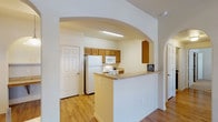 Located in San Antonio, Texas, this single-story residence offers a thoughtfully designed layout that balances comfort and functionality. Warm hardwood-style flooring flows through the main living areas, complemented by neutral walls and ceiling fans that maintain a bright, airy atmosphere throughout.

The living area is generously sized, featuring a ceiling fan with light fixture, a glazed exterior door that allows natural light to filter in, and an elegant arched entryway that connects seamlessly to the kitchen. The kitchen is well-equipped with warm-toned wood cabinetry, light laminate countertops, white appliances including a refrigerator, range, microwave, and dishwasher, and a peninsula-style breakfast bar ideal for casual dining. A pendant light fixture adds a refined touch above the dining area nearby.

The bedrooms are carpeted for comfort and are generously proportioned. The primary bedroom connects directly to an en-suite bathroom featuring a walk-in shower with glass doors, a wood-cabinet vanity with a granite-style countertop, and tile flooring. A spacious walk-in closet with multi-tier wire shelving offers ample storage. A second full bathroom includes a soaking tub and shower combination with matching cabinetry and tile flooring. The layout is practical and well-organized, making efficient use of every area.