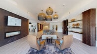 Located at 8337 S Valley Hwy in Englewood, Colorado, this single-floor amenity space offers a generously sized, open-concept layout designed with modern sophistication. The interior is anchored by a welcoming lounge area adorned with striking woven globe pendant lights suspended from a tray ceiling, creating a warm and inviting focal point. Light wood-look tile flooring flows seamlessly throughout, tying the various zones together with a cohesive, contemporary aesthetic.

The main lounge features a curved sofa, leather accent chairs, and a curated display shelf with dark wood slatted panels and decorative objects, adding an artful, boutique quality to the space. A linear fireplace set against a bold dark stone accent wall provides an elegant contrast to the otherwise light and airy palette.

A dedicated dining and collaboration area is bathed in natural light from floor-to-ceiling windows that offer views of the surrounding landscaped grounds. Rustic wood tables paired with plush upholstered chairs and woven pendant lighting create a refined yet relaxed atmosphere ideal for gathering or working.

The full kitchen is outfitted with light wood cabinetry, a striking marble-veined island, white square-tile backsplash, a textured ceiling detail, and a bold black pendant light — combining functionality with high-end design. The space overall exudes a polished, community-focused ambiance throughout.