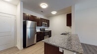 This single-floor residence offers a clean, contemporary design highlighted by consistent finishes throughout. The kitchen is a standout feature, outfitted with rich dark-espresso cabinetry, granite countertops, and a full suite of stainless steel appliances including a refrigerator, range, microwave, and dishwasher. A peninsula with an integrated sink and additional counter space connects the kitchen to the living area, creating an open and functional layout ideal for everyday living and entertaining.

The living area is bright and open, benefiting from natural light through a window fitted with horizontal blinds, and is equipped with a ceiling fan for added comfort. Light wood-tone luxury vinyl plank flooring runs throughout the main living spaces, adding warmth and continuity to the design.

The bedroom is a calm, well-proportioned space with its own window offering views of the surrounding exterior, complemented by wood-tone flooring that adds a sense of coziness. The bathroom is finished with large-format tile flooring, a dark-cabinetry vanity topped with granite, an undermount sink, and a full soaking tub with a tiled surround. Neutral, light-toned walls throughout the residence create a clean, move-in-ready aesthetic that is both versatile and inviting.