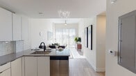 This single-floor residence showcases a clean, contemporary design throughout its thoughtfully laid-out living spaces. The open-concept kitchen and living area serves as the heart of the unit, where light wood-look flooring, crisp white walls, and abundant natural light create a bright, welcoming atmosphere. A floor-to-ceiling sliding glass door floods the living area with sunlight and provides access to an outdoor balcony, while a ceiling fan enhances comfort and airflow.

The kitchen is efficiently designed with tall white cabinetry extending to the ceiling, offering generous storage. A light grey tile backsplash complements the dark countertops, and the space is fully equipped with stainless steel appliances, including a refrigerator, electric range, built-in microwave, and dishwasher. A kitchen island with an undermount sink and matte black faucet doubles as a casual dining or prep area.

The bathroom features a frameless glass walk-in shower, white cabinetry with a stone-toned countertop, an undermount sink, and matte black fixtures throughout for a cohesive modern aesthetic.

Bedrooms are calm and comfortable, with plush carpeting, generous wall space, and large windows that invite in natural light and outdoor views of surrounding greenery.