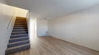 This two-story home in Hewitt, Texas is thoughtfully laid out across two floors, offering a comfortable and functional living arrangement. The main level features light wood-style luxury vinyl flooring throughout the open living room, which is characterized by clean white panel-style walls and a textured ceiling. The living room flows naturally toward the kitchen, which is equipped with crisp white cabinetry, a double-basin sink, and black appliances including a refrigerator, electric range, and over-the-range microwave. A window provides natural light to the kitchen area. Also on the main floor is a full bathroom featuring a white vanity with storage, light countertops, and light wood-style flooring. Carpeted stairs lead to the upper level, where both bedrooms are located. The primary bedroom offers generous proportions with its own closet, while the secondary bedroom is equally well-sized. Both rooms feature neutral carpet, white panel walls, and textured ceilings. A second full bathroom on the upper level mirrors the clean, white aesthetic of the home with a matching vanity and light flooring. Additional conveniences include a dedicated laundry area, hallway, and two closets distributed throughout the home, making efficient use of the overall footprint.