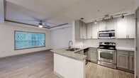 Located at 1970 Peachford Rd in Dunwoody, Georgia, this single-floor residence offers a well-designed open layout with modern finishes throughout. Light wood-tone flooring runs continuously across the living areas, bedrooms, and kitchen, creating a cohesive and clean aesthetic.

The open-concept kitchen serves as a central hub, featuring granite countertops, a peninsula with a built-in sink, stainless steel appliances including a range and microwave, and grey shaker-style cabinetry with a subway tile backsplash. The kitchen flows seamlessly into the living area, which is highlighted by a tray ceiling with a ceiling fan and multiple windows that frame lush greenery views, filling the space with natural light.

The bedrooms continue the tray ceiling design and ceiling fan fixtures, each with large windows offering wooded outdoor views. One bedroom includes a spacious walk-in closet outfitted with wire shelving and hanging rods. The bathroom features wood-look tile flooring, white subway tile walls in the shower area, and a glass shower partition alongside a separate soaking tub. Track lighting in the kitchen and living areas adds a modern, functional touch. The overall ambiance is bright, neutral, and move-in ready.