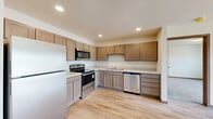 Located at 1330 Main Ave in Moorhead, MN, this one-bedroom, one-bathroom unit offers a functional and well-appointed single-floor layout. The combined kitchen and living room serves as the heart of the unit, featuring light wood-style luxury vinyl plank flooring that carries a clean, modern aesthetic. The kitchen is equipped with stainless steel appliances — including a refrigerator, range, microwave, and dishwasher — complemented by warm-toned wood cabinetry, light countertops, and recessed lighting. The living area is bright and open, anchored by sliding glass doors that lead to a private balcony with outdoor views, allowing natural light to fill the space. Baseboard heating runs along the perimeter walls, providing efficient warmth throughout. The bedroom offers a comfortable footprint with plush carpeting, a sliding window with exterior views, and ample wall space. The bathroom includes a walk-in shower with a clean white surround and chrome fixtures. A dedicated in-unit laundry area houses a stacked washer and dryer with overhead shelving, adding everyday convenience. The unit's neutral color palette and practical layout make it a well-organized and move-in-ready living space.