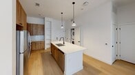 Located in Aurora, CO, this well-designed one-bedroom, one-bathroom home offers a thoughtfully organized single-floor layout with modern finishes throughout. The open-concept living and kitchen area is anchored by a striking kitchen island with a white quartz countertop, undermount sink, and matte black fixtures, illuminated by pendant lighting above. Warm wood-toned cabinetry lines the kitchen walls, complemented by a white subway tile backsplash, stainless steel appliances including a range with over-the-range microwave, and a built-in dishwasher. Light hardwood flooring flows throughout the main living areas, creating a clean, airy aesthetic. Built-in open shelving adds functional charm near the kitchen. The living area features a glass-panel exterior door that allows natural light to fill the space. The bedroom is finished with plush carpet and crisp white walls, offering a calm retreat. The bathroom is appointed with a wide wood-vanity, dual sinks with matte black fixtures, a large framed mirror, and a linen-style tall cabinet for additional storage. An in-unit stacked washer and dryer adds everyday convenience. The overall design balances modern minimalism with warm, natural materials for a cohesive and inviting feel.