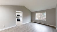 Located at 558 121st Pl NE in Bellevue, WA, this one-bedroom, one-bathroom unit offers a thoughtfully designed layout with modern finishes throughout. The living room is a standout space, featuring striking vaulted ceilings and light-toned hardwood-style flooring that lend an open, airy feel. A large sliding window frames views of the surrounding neighborhood and greenery, while a baseboard heating system ensures year-round comfort. The combined dining and kitchen area is well-appointed with white shaker-style cabinetry, subway tile backsplash, gray countertops, and a full suite of stainless steel appliances including a refrigerator, range, microwave, and dishwasher. Light vinyl plank flooring continues throughout this space. The bedroom is generously sized, finished with plush carpeting, a large window with outdoor views, and access to two closets. The bathroom features a white subway tile tub/shower surround, a vanity with gray countertop, white cabinetry, and matte black hardware accents. Additional highlights include a private balcony, a dedicated entrance, and a neutral gray palette throughout that creates a clean, cohesive aesthetic.