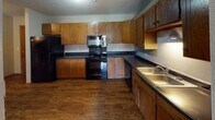 Located at 3401 W 51st St in Sioux Falls, South Dakota, this single-floor unit offers a practical and comfortable layout designed for everyday living. The living area is finished with plush carpeting and neutral-toned walls, creating a bright and welcoming atmosphere. A sliding glass door fitted with vertical blinds opens to an outdoor balcony, allowing natural light to filter in and providing a pleasant outdoor connection. A convenient pass-through window connects the living area to the kitchen, adding an open feel between the two spaces. The kitchen is well-equipped with warm wood cabinetry, dark countertops, wood-look flooring, and black appliances including a range, microwave, refrigerator, and dishwasher, along with a double-basin sink. The bedrooms are carpeted and generously sized, with one featuring a ceiling fan with integrated lighting and a window that brings in natural light, and another offering a closet with built-in shelving. The bathroom includes a combination tub and shower, a vanity with dark countertops, wood cabinetry, and wood-look flooring. Textured ceilings and warm wood-toned baseboards are consistent throughout, lending a cohesive character to the entire space.