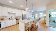Located at 7045 Pine Forest Rd in Pensacola, FL, this well-appointed 1-bedroom, 1-bathroom residence offers a thoughtfully designed open-concept layout that maximizes every square foot. The combined kitchen and living area forms the heart of the home, anchored by a central granite-topped island with bar seating and elegant pendant lighting overhead. The kitchen is outfitted with crisp white shaker cabinetry, a classic subway tile backsplash, and a full suite of stainless steel appliances including a refrigerator, range, microwave, and dishwasher. Light hardwood flooring flows seamlessly throughout the main living areas, complementing the neutral, warm color palette. The living room is bright and inviting, featuring a ceiling fan, recessed lighting, and a glass-paned door that opens to a private outdoor balcony, allowing for generous natural light. The bedroom offers plush carpeting, a ceiling fan, and a window with outdoor views, along with direct access to a dedicated walk-in closet with built-in shelving. The bathroom continues the home's refined aesthetic with white cabinetry, a granite vanity, a tiled tub-shower combination, and hardwood-style flooring. Clean lines, consistent finishes, and abundant natural light create a cohesive and comfortable living environment throughout.