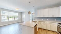 Located at 5 Lakeshore Center in Bridgewater, MA, this thoughtfully designed 2-bedroom, 2-bathroom residence offers a comfortable and modern living experience across a single floor. The open-concept layout connects the living room and kitchen seamlessly, with light-toned luxury vinyl plank flooring running throughout the main living areas.

The kitchen is a standout feature, showcasing crisp white shaker-style cabinetry, a soft blue glass tile backsplash, stone countertops, and a central island with a stainless steel sink. A full suite of stainless steel appliances — including a gas range, microwave, refrigerator, and dishwasher — complete the space. Stylish pendant lights hang above the island, enhancing the kitchen's contemporary aesthetic.

The primary bedroom is generously sized with plush carpeting and direct access to an en-suite bathroom featuring a glass-enclosed walk-in shower with large-format tile, a granite-topped vanity, and white cabinetry. The second bedroom offers hardwood-style flooring and a wide window with peaceful green views. The second bathroom includes a tiled tub-shower combination and matching white vanity finishes. Hallways provide double-door closet storage, adding practical functionality to this well-planned home.