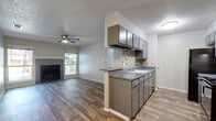 This single-floor, 2-bedroom, 1-bathroom residence offers a practical and cohesive layout designed for comfortable everyday living. Throughout the home, wood-look plank flooring and soft gray-toned walls create a clean, modern aesthetic that ties each room together.

The combined kitchen and living area forms the heart of the home. The living room features a tiled fireplace flanked by windows that invite natural light, complemented by a ceiling fan overhead. The galley-style kitchen is efficiently designed with gray cabinetry, gray countertops, mosaic tile backsplash, and black appliances including a range and refrigerator. A built-in shelving unit near the entryway adds convenient storage.

Both bedrooms are well-sized and include ceiling fans. The primary bedroom offers sliding glass door access to a private balcony with outdoor views, while the second bedroom features a large closet and a window with natural light. Each bedroom benefits from a calm, neutral palette.

The bathroom is equipped with gray cabinetry, a wide vanity with a solid-surface countertop, a tub-shower combination with tile surround, and wood-look flooring that continues the home's consistent design language. The textured ceilings are present throughout, adding a classic residential character to the overall space.