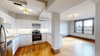 This well-appointed 1-bedroom, 1-bathroom residence combines classic character with modern updates throughout its thoughtfully designed single-floor layout. Warm hardwood floors flow continuously through every room, complemented by rich dark wood trim, baseboards, and six-panel doors that add timeless architectural detail.

The kitchen serves as a standout feature, offering white shaker cabinetry with gold hardware, granite countertops, a classic white subway tile backsplash, and a full suite of stainless steel appliances including a refrigerator, dishwasher, and range. The kitchen opens naturally to the dining area, creating a functional and connected living space anchored by a structural column that adds to the unit's character.

The bedroom is a quiet, comfortable retreat bathed in natural light from large, dark-framed windows that frame urban skyline views. The richly stained window surrounds echo the home's classic aesthetic.

The bathroom is a design highlight, featuring sage green wainscoting, a white pedestal sink, polished gold fixtures and accessories, a gold-framed mirror, and a subway-tiled walk-in shower with a glass enclosure — a refined combination of vintage charm and contemporary style.