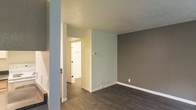 This two-story space offers a contemporary and well-maintained interior defined by a neutral color palette and cohesive design choices throughout. The flooring features rich, dark hardwood-style planks that run consistently across the main living areas, grounding the space with a warm yet modern aesthetic.

The walls are finished in a combination of soft gray-blue and deeper taupe tones, lending each area a calm, understated character. Crisp white baseboards and trim provide clean contrast against both the wall colors and the flooring, contributing to a polished, finished look. The ceilings are smooth with a subtle texture, maintaining a bright and open feel across the rooms.

The layout is open and functional, with clear sightlines between connected areas that enhance the sense of flow. Doorways lead between rooms with natural light filtering through, brightening the interior and highlighting the clean finishes. Electrical outlets and wall plates are neatly integrated throughout, reflecting attention to practical detail.

Spanning two floors, the space provides a clear separation between living areas, offering both communal and private zones. The overall ambiance is modern, neutral, and move-in ready, making it a versatile space well-suited to a variety of uses and interior styles.