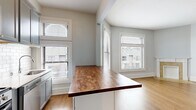 Located in the Lowry Hill neighborhood of Minneapolis, this one-bedroom, one-bathroom unit offers a well-designed layout across a single floor. The open-concept living room and kitchen area is anchored by warm hardwood flooring and abundant natural light streaming through multiple windows with classic white trim. A decorative fireplace with a tile surround and white mantel serves as a focal point in the living room, adding character to the space.

The kitchen is thoughtfully appointed with gray shaker-style cabinetry, subway tile backsplash, stainless steel appliances including a gas range and microwave, and a peninsula featuring a rich butcher block countertop — ideal for both meal prep and casual dining.

The bedroom is a comfortable size, carpeted for warmth, and includes a window that brings in natural light. It connects conveniently to the bathroom, which is finished with gray shaker vanity cabinetry, a subway tile walk-in shower, mosaic tile flooring, and a mirrored medicine cabinet. A hallway connects the main living areas to the private spaces, maintaining a practical and efficient flow throughout. The soft gray palette used throughout the unit creates a cohesive, calm ambiance.