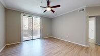 This single-story residence presents a cohesive, modern interior finished in a neutral gray palette throughout. Light wood-style flooring extends across the main living areas and entryway, complementing the crown molding and clean white baseboards that frame each room. The living area is highlighted by a ceiling fan, crown molding, and a sliding glass door fitted with vertical blinds that opens to an outdoor view, allowing natural light to fill the space.

The kitchen is well-appointed with gray shaker-style cabinetry, granite countertops, a white subway tile backsplash, and a full suite of stainless steel appliances, including a refrigerator, range, microwave, and dishwasher. A peninsula provides additional counter space and casual seating. An in-unit laundry closet is conveniently located adjacent to the kitchen.

The bedrooms feature plush wall-to-wall carpeting and ceiling fans, each with windows fitted with blinds that bring in natural light. Two bathrooms serve the unit: one includes a soaking tub with tiled surround, and the other offers a walk-in shower. Both bathrooms feature gray cabinetry with brushed hardware, granite countertops, and wood-style tile flooring. The primary bath includes a dual-sink vanity with a large mirror and bright overhead lighting.