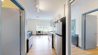Located at 2915-2949 N Forest Rd in Getzville, NY, this efficiently designed studio unit offers a thoughtful layout across a single floor. The space features light-toned hardwood flooring throughout, clean white walls, and blue accent trim that lends a modern, cohesive aesthetic.

The kitchen is well-appointed with granite countertops, grey cabinetry, and a full suite of stainless steel appliances including a refrigerator, electric range, built-in microwave, and dishwasher. Ample upper and lower cabinet storage maximizes functionality within the compact footprint. A small seating area adjacent to the kitchen provides a comfortable living space, with track lighting overhead.

The sleeping area is bright and inviting, featuring a large window that frames lush green outdoor views and fills the room with natural light. The space accommodates a platform bed with built-in drawer storage and a desk with chair, making it practical for both rest and work.

The bathroom is clean and modern, finished with a granite-top vanity, white cabinetry, and a large mirror. Light hardwood flooring continues here, complementing the crisp white walls. A grab bar adds an accessible design touch. This unit is ideal for those seeking a functional, well-finished space in a residential setting.