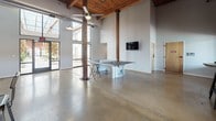 Located at 1650 Overbrook Rd in Richmond, VA, this single-floor space masterfully blends industrial character with modern amenities. The architecture is defined by soaring ceilings with warm wood beam accents, exposed structural columns, and original brick walls that lend a raw, authentic aesthetic throughout. Polished concrete floors unify the expansive open layout, reflecting natural light that pours in through floor-to-ceiling windows and glass doors.

The main gathering area is a standout, offering generous open floor space ideal for events or recreation, complete with a ping pong table, wall-mounted TV, and ceiling fans that enhance comfort. A separate lounge area features mid-century modern seating arranged on a vintage-style area rug, providing a more intimate retreat within the larger space.

The well-appointed kitchen is a functional highlight, boasting granite countertops on dual runs of cabinetry, subway tile backsplash, stainless steel appliances, and pendant lighting—all framed by the characteristic exposed brick walls. An adjacent bar area with a granite-topped island and industrial-style bar seating creates a natural hub for socializing.

A large open room with original brick walls, barn-style sliding doors, polished floors, and industrial bar-height tables rounds out the space, offering flexible room for gatherings or events.