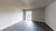 This single-floor residence offers a thoughtfully designed layout that balances comfort and functionality throughout. The open living area is finished with durable wood-style flooring and neutral-toned walls, creating a bright, versatile space. A sliding glass door leads directly to a private balcony with a railed surround, allowing natural light to fill the room and providing pleasant outdoor views. The kitchen is positioned adjacent to the living area and features white shaker-style cabinetry, granite countertops, stainless steel appliances including a range and refrigerator, a stainless range hood, and matching wood-style flooring — offering a clean, modern aesthetic. The bedrooms are carpeted for warmth and comfort, each featuring neutral walls, a textured ceiling, and windows that allow in natural light. One bedroom includes a dedicated walk-in closet outfitted with white wire shelving on multiple levels, providing ample storage. The bathroom is finished with a white vanity, granite countertop, and wood-style flooring, maintaining a consistent, updated look throughout. Textured ceilings are present across the home, and the overall neutral color palette creates a cohesive and move-in-ready environment suitable for a range of living arrangements.