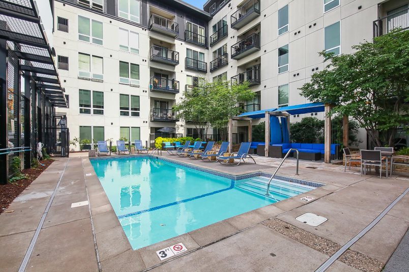 Apartment complex outdoor swimming pool and hot tub with lounge chairs and cabana.