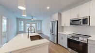 Located on Nexus Ave in Stafford, TX, this thoughtfully designed one-bedroom, one-bathroom residence offers a clean, modern aesthetic across a single floor. The open-concept kitchen and living area serves as the heart of the home, showcasing white shaker-style cabinetry, light gray lower cabinets, white quartz countertops, a subway tile backsplash, and a full suite of stainless steel appliances including a French door refrigerator, electric range, built-in microwave, and dishwasher. A center island with a deep farmhouse sink and pendant lighting above adds both functionality and visual appeal. The living area is bright and airy, benefiting from large windows and glass French doors that invite natural light and provide outdoor views, complemented by a ceiling fan overhead. Warm wood-look flooring flows throughout the main living spaces, while the bedroom features plush carpeting, a ceiling fan, and a window overlooking the exterior. The bathroom is finished with marble-style tile surrounding the tub and shower, a wide white vanity with an illuminated mirror, and matching wood-look flooring. An in-unit stacked washer and dryer and a dedicated closet round out the practical offerings of this well-appointed residence.