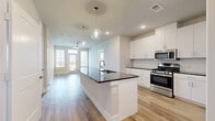 Located in Leander, TX, this well-appointed 2-bedroom, 2-bathroom residence offers a thoughtfully designed single-level floor plan with a clean, modern aesthetic throughout. The open-concept kitchen and living area serves as the heart of the home, featuring light wood-style flooring, crisp white cabinetry extending to the ceiling, dark granite countertops, a subway tile backsplash, and stainless steel appliances including a gas range and French door refrigerator. The living area is bathed in natural light from large windows and a glass door that opens to a private balcony with sweeping, unobstructed views of the Texas Hill Country — a true standout feature of this residence. Both bedrooms are carpeted and equipped with ceiling fans and windows framing lush greenery outside. The primary bedroom includes a generously sized walk-in closet with dual clothing rods and built-in shelving. The primary bathroom showcases a dark granite dual vanity with white cabinetry, wood-style flooring, and a tiled shower-tub combination. Neutral tones, clean lines, and consistent finishes create a cohesive and inviting ambiance throughout the entire space.