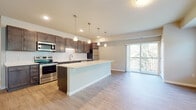 This well-designed single-floor residence offers a thoughtfully laid-out open-concept living space that seamlessly connects the kitchen, dining, and living areas. The kitchen is a standout feature, boasting rich dark-wood cabinetry, a classic white subway tile backsplash, stainless steel appliances, and a generous island with a crisp white countertop illuminated by a row of elegant pendant lights. The kitchen flows naturally into the living area, which is finished with warm wood-look flooring and leads to a private balcony through a sliding glass door, offering pleasant views of surrounding greenery. The bedrooms feature plush carpeting and large windows that invite abundant natural light and outdoor views. The primary bathroom is appointed with a glass-enclosed walk-in shower, a dark-wood vanity with white countertops, brushed nickel fixtures, and a large mirror. A secondary bathroom includes a full soaking tub and shower combination. The unit also benefits from an in-unit washer, adding everyday convenience. Throughout the residence, neutral tones, clean lines, and consistent finishes create a cohesive, modern aesthetic suited for comfortable living.
