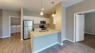 This single-floor residence offers a thoughtfully designed layout that balances functionality and comfort. The kitchen is a standout feature, showcasing granite countertops, crisp white cabinetry with brushed nickel hardware, and stainless steel appliances including a refrigerator, range, microwave, and dishwasher. A peninsula with pendant lighting and an undermount sink adds both style and convenience, opening seamlessly into the living and dining areas. The living space is finished with durable wood-look flooring and features a ceiling fan, with sliding glass doors leading to a private balcony offering pleasant outdoor views and natural light. The bedrooms are carpeted for comfort, each featuring ceiling fans and windows with blinds that allow ample daylight. The primary bathroom is well-equipped with a granite-topped vanity, a large wall mirror, warm sconce lighting, and a walk-in glass-enclosed shower. A spacious walk-in closet with wire shelving provides generous storage. A secondary bathroom is conveniently accessible from the hallway, which also connects to the additional bedroom. Throughout, neutral warm-gray tones, white trim, and wood-look flooring create a cohesive and inviting atmosphere.