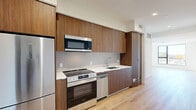 This contemporary 570 square foot apartment in Los Angeles offers a harmonious blend of style and functionality. The open-concept layout maximizes the use of space, creating a seamless flow between the living areas. The kitchen is a standout feature, boasting sleek wood cabinetry, stainless steel appliances, and a clean white backsplash. The living room is bathed in natural light thanks to large windows that offer stunning city views. The bedroom, measuring 120 square feet, includes a mirrored closet door, enhancing the sense of space. The bathroom is modern and minimalist, with a large tiled shower and neutral color palette. Throughout the apartment, light wood flooring adds warmth and continuity. Recessed lighting and high ceilings contribute to the airy feel of the space. This well-designed urban dwelling perfectly balances comfort and sophistication, ideal for those seeking a stylish home in the heart of Los Angeles.