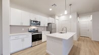 Located at 2121 N 99th Ave in Phoenix, AZ, this well-appointed one-bedroom, one-bathroom residence offers a thoughtfully designed single-floor layout with modern finishes throughout. The open-concept kitchen and living area serves as the heart of the home, featuring light wood-style flooring, crisp white cabinetry, a subway tile backsplash, and a central island with a quartz countertop and undermount sink. Stainless steel appliances — including a range, microwave, and refrigerator — complete the kitchen, which is illuminated by stylish pendant lighting. The living area flows seamlessly toward a sliding glass door that opens to a private balcony, offering outdoor views of the surrounding landscape. The bedroom is a comfortable retreat featuring plush carpeting, a ceiling fan, and multiple windows with blinds that fill the room with natural light. A dedicated closet provides convenient storage. The bathroom is clean and contemporary, outfitted with a quartz vanity, white cabinetry, wood-look flooring, and a glass-enclosed walk-in shower. Additional spaces include a pantry and hallway, contributing to the home's efficient and functional layout. The overall ambiance is bright, clean, and move-in ready.
