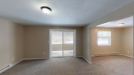 This single-floor unit in Cicero, NY is designed with a practical, straightforward layout that maximizes functionality throughout. The living area is a comfortable, open space finished with wall-to-wall carpeting and neutral beige walls. A large sliding glass door serves as a focal point, filling the room with natural light and providing access to an outdoor area. An adjacent windowed space extends the living area, offering additional flexibility. Baseboard heating is present throughout, ensuring efficient warmth during Central New York winters.

The kitchen is equipped with warm-toned wooden cabinetry offering ample upper and lower storage, white laminate countertops, and a white electric range with overhead ventilation. The layout provides a practical workflow for everyday cooking needs.

The bedrooms are generously proportioned, each featuring soft carpeting, neutral walls, windows that admit natural light, and baseboard heaters. One bedroom includes access to a full bathroom, which is outfitted with a single-sink vanity with wood cabinetry, a mirror, and a tub-shower combination with a grab bar. A sizable closet with double sliding doors adds convenient storage to the living space. Overall, the unit presents a clean, move-in ready environment in a residential Cicero location.