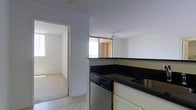 This single-floor space is designed with a functional, open layout that connects the kitchen to the adjacent living area. The kitchen features dark countertops that contrast with white cabinetry, providing ample workspace. A stainless steel dishwasher is integrated beneath the counter, and a sink is conveniently positioned nearby. A defining architectural feature is the pass-through window or bar-height counter opening, which visually connects the kitchen to the living space, enhancing the sense of openness and allowing natural light to flow throughout.

The flooring transitions from tile in the kitchen to carpet in the living area, clearly delineating the two spaces. The living area benefits from a ceiling fan, which aids in air circulation, as well as a window that allows natural light to brighten the room. Walls throughout are finished in a clean, neutral white, creating a versatile backdrop. The overall ambiance is practical and straightforward, with a layout that maximizes the use of available space on a single level.