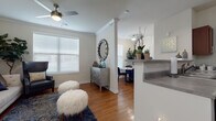 This thoughtfully designed single-floor residence offers a comfortable and cohesive living experience, with warm hardwood flooring flowing through the main living and kitchen areas. The open-concept living room is highlighted by crown molding, a ceiling fan, and multiple windows with white blinds that invite ample natural light. A decorative column partially divides the living space from the dining area, maintaining an airy, connected feel. A breakfast bar extends from the kitchen, providing additional counter space and a casual seating option.

The galley-style kitchen is well-equipped with rich cherry wood cabinetry, gray countertops, a double sink, and black appliances including a range and microwave. A door from the kitchen leads directly to an in-unit laundry area, adding everyday convenience.

The space includes two carpeted bedrooms, each featuring large windows and soft, neutral tones. The primary bedroom is generously sized and benefits from access to a spacious walk-in closet outfitted with wire shelving along multiple walls. The full bathroom features large-format tile flooring, a rich wood vanity with ample storage, a wide mirror, and a soaking tub. Crown molding and consistent warm-toned finishes tie the space together with a polished, cohesive aesthetic throughout.