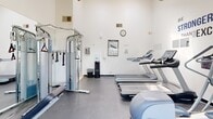 Located at 395 Ano Nuevo Ave in Sunnyvale, CA, this fitness center is a well-equipped, single-floor exercise facility designed to support a range of workout routines. The space is divided into two exercise areas, together offering a comprehensive selection of equipment within a compact yet efficiently organized footprint.

The main workout area features vaulted ceilings that lend a sense of openness, while a ceiling fan aids in air circulation during exercise. Large windows along one wall flood the room with natural light and offer views of the surrounding greenery and outdoor courtyard, creating an inviting atmosphere. Motivational wall decals — including the phrases "Be Stronger Than Your Excuses" and "Dedication" — reinforce the space's energetic character.

Cardio equipment includes multiple treadmills and elliptical machines from brands such as Precor and Spirit, arranged to make efficient use of the floor space. A Paramount cable strength machine and a free weight rack with dumbbells provide options for resistance training. Rubber flooring throughout both exercise rooms ensures safety and durability.

A tiled entryway with a mat, hand sanitizer station, and informational bulletin board provides a clean transition into the facility. A water dispenser and wall clock are also present, adding practical convenience. Full-length mirrors help users monitor their form, completing this functional and motivating fitness environment.