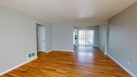 This single-floor residence offers a clean, functional layout designed for comfortable everyday living. The open living and dining area is defined by warm-toned hardwood flooring that flows throughout the space, complemented by soft grey walls and a textured ceiling. A large sliding glass door with vertical blinds allows abundant natural light to fill the living area, creating a bright and welcoming ambiance.

The galley-style kitchen features white cabinetry with ample storage, dark countertops, stainless steel appliances including a full-size refrigerator, and a double-basin sink beneath a window. The light wood-look flooring ties the kitchen seamlessly into the rest of the home.

Multiple bedrooms are present, each showcasing the same rich hardwood flooring, neutral grey walls, and wide windows fitted with vertical blinds that invite natural light. The rooms offer a versatile and airy feel well-suited for a variety of uses.

The bathroom is finished with white tile surrounding a full soaking tub and shower, white cabinetry, dark countertops, and a window above the tub for natural ventilation and light. The flooring continues the home's cohesive tile and wood aesthetic. Overall, the space presents a tidy, move-in-ready environment with consistent finishes throughout.