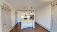 This single-floor unit offers a thoughtfully designed layout that balances modern style with everyday functionality. The open-concept living and kitchen area is anchored by rich, dark hardwood flooring that flows throughout. A sliding glass door fills the living space with natural light and provides access to a private balcony, while a ceiling fan adds comfort overhead.

The kitchen is a standout feature, showcasing floor-to-ceiling white shaker cabinetry with glass-front accents, a white subway tile backsplash, and a full suite of stainless steel appliances including a range, built-in microwave, and French door refrigerator. A central island with a light countertop and undermount sink serves as both a prep space and casual gathering spot, illuminated by two stylish brass globe pendant lights.

The bedroom is finished with plush carpet and dual windows that invite natural light and outdoor views, complemented by a ceiling fan for added airflow. The bathroom is finished with neutral-toned tile surrounding a soaking tub and shower combination, paired with a white vanity, built-in storage cabinetry, and access to a walk-in closet. The overall aesthetic is clean and contemporary, with warm brass hardware accents tying the design together throughout the space.