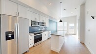 Located in Denver's vibrant North City Park neighborhood, this efficiently designed one-bedroom, two-bathroom residence offers a thoughtfully laid-out single-floor plan with modern finishes throughout. Light-toned hardwood flooring flows seamlessly across the entire space, complementing the bright, open atmosphere created by tall ceilings and large windows.

The kitchen is a standout feature, showcasing crisp white shaker cabinetry, a textured blue tile backsplash, stainless steel appliances including a side-by-side refrigerator and range, a built-in microwave, and a dishwasher. A white island with a dark countertop provides additional workspace and casual seating, anchored by a sleek pendant light above.

The open living area is bathed in natural light and features a striking teal accent wall. A glass door leads to a private balcony offering sweeping views of the Denver skyline — a rare highlight that brings the city's energy directly into the home.

The bedroom is a well-proportioned retreat with direct access to the main living area. Both bathrooms are finished in clean white tones with dark matte hardware, one featuring a full soaking tub and shower combination. A dedicated laundry area with a stacked washer and dryer and a walk-in closet with wire shelving add practical convenience to this polished urban residence.