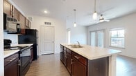 This single-floor, 1-bedroom, 1-bathroom unit is thoughtfully designed to maximize functionality and comfort. The open-concept living and kitchen area serves as the heart of the space, anchored by a central island with a built-in sink, light countertops, and rich dark-wood cabinetry. Pendant lighting hangs above the island, complementing the recessed ceiling lights and a ceiling fan that together create a bright, well-ventilated atmosphere. Black appliances, including a refrigerator, range, and microwave, complete the kitchen. Hardwood-style flooring runs throughout the main living area, adding warmth and visual continuity.

The bedroom offers a comfortable and private retreat, featuring plush carpeting, a ceiling fan, and a window that invites natural light and outdoor views. Two closets provide generous storage space, each equipped with built-in wire shelving for organized use.

The bathroom is finished with tile-surround tub and shower combination, wood-style flooring, and dark cabinetry with light countertops that echo the kitchen's design palette. A hallway connects the rooms efficiently, contributing to the unit's clean, practical layout. Overall, the space presents a cohesive and modern aesthetic throughout.