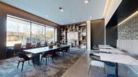 Located at 300 N Willson Ave in Bozeman, Montana, this Lobby Lounge is a thoughtfully designed communal space that blends modern aesthetics with functional versatility. The single-floor layout flows seamlessly across a generously sized footprint, anchored by polished concrete flooring that reflects recessed lighting throughout.

The main lounge area features a large, dark wood conference-style table surrounded by contemporary chairs, positioned to take full advantage of expansive floor-to-ceiling windows that flood the space with natural light and offer views of the surrounding streetscape. A striking built-in shelving unit with warm wood tones serves as a focal point, framing a central display panel and decorative objects.

A banquette seating zone provides an intimate dining or gathering area, with upholstered booth-style benches set against a textured tile accent wall illuminated by warm LED cove lighting. Separate lounge seating clusters, furnished with sleek armchairs and side tables, offer additional spaces for casual interaction or relaxation.

The entry vestibule features a sophisticated glass-and-steel door system flanked by stone-clad columns, establishing an elegant arrival experience. Connecting hallways with warm wood-paneled ceilings and curated artwork guide occupants through the space. The overall ambiance is contemporary and polished, balancing professional functionality with welcoming comfort.