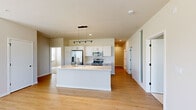 Located at 3200 Northwoods Rd in Saukville, WI, this well-designed single-floor home offers 2 bedrooms and 2 bathrooms with a clean, modern aesthetic. The open-concept kitchen and living area serves as the heart of the home, showcasing white shaker cabinetry, gleaming white quartz countertops, and a generously sized center island with a built-in sink. Stainless steel appliances—including a French door refrigerator, electric range, and microwave—add a polished, contemporary feel, while track and pendant lighting accent the space. Light-toned hardwood-style flooring runs throughout the main living areas, enhancing the bright, airy atmosphere. The living area offers direct access to the outdoors through a glass-panel door, inviting natural light and outdoor views. The primary bedroom is a comfortable retreat featuring soft carpeting, a spacious sliding-door closet, and an en-suite bathroom complete with a double-sink vanity, white cabinetry, and a glass-enclosed walk-in shower. The second bedroom is equally well-appointed, with plush carpeting and multiple large windows that frame lush outdoor greenery. The second bathroom maintains the same refined style with white cabinetry and wood-look flooring. Throughout, neutral tones and black hardware accents tie the design together cohesively.
