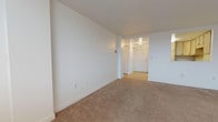 Located at 48 Holy Family Rd in Holyoke, Massachusetts, this single-floor residence offers a well-organized layout designed for comfortable everyday living. The living area is generously sized, finished with neutral wall-to-wall carpeting and crisp white walls that create a clean, bright atmosphere. A distinctive pass-through window connects the living space to the kitchen, enhancing the sense of openness between the two areas. The kitchen is equipped with light wood cabinetry offering ample storage, a double-basin sink, smooth countertops, a dishwasher, an electric range, and a built-in microwave, all set on tile flooring. The bedroom is spacious and carpeted, featuring a window with outdoor views that brings in natural light, along with a dedicated walk-in closet fitted with wire shelving for organized storage. Two bathrooms serve the unit; one includes a full tub-shower combination with tile flooring and a wood-cabinet vanity with a mirror, while a second bathroom also features a tub-shower enclosure with tile flooring. A entry hallway connects the main living spaces, and the overall layout, as seen in the 3D model, is efficiently arranged to maximize usable space throughout.