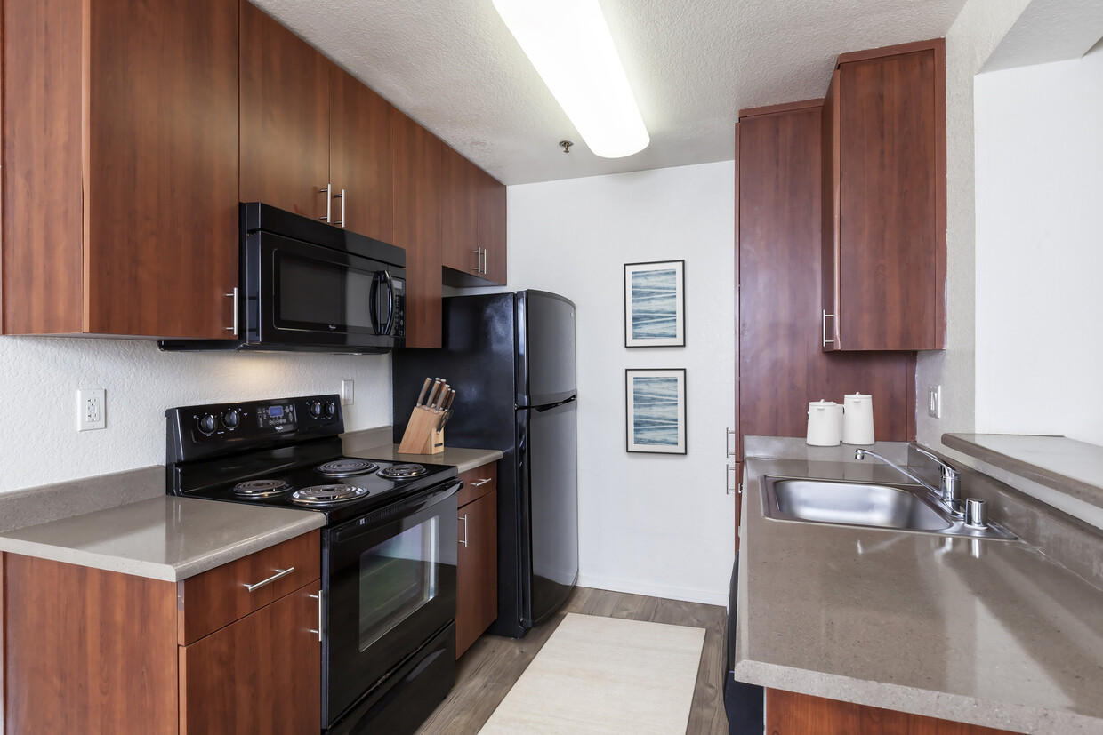 Cocina con gabinetes de madera de cerezo, encimeras de color gris claro, electrodomésticos de color negro y pisos de superficie dura - eaves Pleasanton