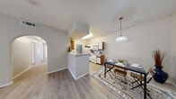 This single-floor residence offers a thoughtfully designed layout that balances functionality with comfortable living. The open-concept kitchen and dining area serves as the heart of the home, featuring a peninsula with a white countertop that provides additional prep space and a natural divider between the two areas. The kitchen is equipped with white appliances including a refrigerator, electric range, and over-the-range microwave, complemented by two-tone wood and white cabinetry offering ample storage. A pendant light fixture illuminates the adjacent dining space, which is framed by a graceful archway leading to the rest of the home. Light wood-look laminate flooring runs consistently throughout, lending a clean and cohesive feel to every room. The bedrooms are generously proportioned, each featuring ceiling fans with integrated lighting and windows that invite natural light. A full bathroom includes a tub-shower combination with white tile surround, a vanity with storage, and matching laminate flooring. A separate water closet provides added privacy and convenience. The utility room offers wire shelving and in-unit washer/dryer hookups. The entry area is open and welcoming, completing this practical and well-appointed single-story residence.