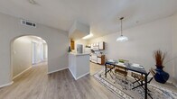 This single-floor residence offers a thoughtfully designed layout that balances functionality with comfortable living. The open-concept kitchen and dining area serves as the heart of the home, featuring a peninsula with a white countertop that provides additional prep space and a natural divider between the two areas. The kitchen is equipped with white appliances including a refrigerator, electric range, and over-the-range microwave, complemented by two-tone wood and white cabinetry offering ample storage. A pendant light fixture illuminates the adjacent dining space, which is framed by a graceful archway leading to the rest of the home. Light wood-look laminate flooring runs consistently throughout, lending a clean and cohesive feel to every room. The bedrooms are generously proportioned, each featuring ceiling fans with integrated lighting and windows that invite natural light. A full bathroom includes a tub-shower combination with white tile surround, a vanity with storage, and matching laminate flooring. A separate water closet provides added privacy and convenience. The utility room offers wire shelving and in-unit washer/dryer hookups. The entry area is open and welcoming, completing this practical and well-appointed single-story residence.