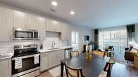 Located at 5401 Atlantic Springs Rd in Raleigh, NC, this single-story clubhouse serves as the social and amenity hub of the Atlantic Springs community. The space is designed with a contemporary aesthetic, showcasing light large-format tile flooring, crisp white walls, and bold exposed black ceiling beams that create a striking visual contrast throughout.

Guests enter through floor-to-ceiling black-framed glass doors that flood the entryway with natural light and offer immediate views of the surrounding community. The main lounge area is anchored by a dramatic wood-clad fireplace column with a large mounted flat-screen display above, flanked by generous seating arrangements and a statement chandelier. Expansive grid-pane windows line the rear wall, providing unobstructed views of the outdoor pool area and bringing the outside in.

Adjacent to the lounge is a stylish café-style bar with white countertops, bar seating, pendant lighting, and a slatted wood accent wall, ideal for casual gatherings. A dedicated coworking alcove features built-in desk space, wall-mounted screens, and large windows, offering a functional workspace with outdoor views. Additional seating nooks with upholstered banquettes provide more intimate settings. The shuffleboard table and open social areas round out a clubhouse designed to foster both relaxation and community engagement.
