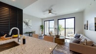 Located in Miami's vibrant 33133 zip code, this contemporary single-floor residence offers a thoughtfully designed open-concept layout that seamlessly connects the kitchen, dining, and living areas. The kitchen is outfitted with rich dark wood cabinetry, granite countertops, stainless steel appliances, a subway tile backsplash, and warm hardwood flooring that extends throughout the main living spaces.

The living room is a standout, anchored by floor-to-ceiling black-framed sliding glass doors that flood the space with natural light and open directly onto a private balcony. The balcony offers expansive, panoramic views of the Miami skyline and lush tree canopy, making it a defining feature of the residence. A ceiling fan adds comfort to this bright, airy space.

The bedroom is a serene retreat featuring hardwood floors, black-framed windows with outdoor views, a ceiling fan, and a full-length mirror. Two well-appointed bathrooms complete the residence — one featuring a deep soaking tub with warm-toned tile surround and a granite vanity, and the other offering a frameless glass-enclosed walk-in shower with matching finishes. Both bathrooms showcase large-format marble-style porcelain tile flooring and dark wood vanities with under-mount sinks.