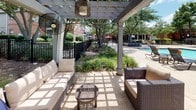 Located at 5270 Bryant Irvin Rd in Fort Worth, Texas, this single-level outdoor amenity space offers a well-appointed community retreat designed for relaxation and recreation. At the heart of the space is a sparkling resort-style swimming pool, bordered by a spacious concrete pool deck furnished with lounge chairs and side tables — ideal for soaking up the Texas sun. Adjacent to the pool, a pergola-covered lounge area provides a shaded escape, featuring wicker sectional sofas with plush cushions, accent chairs, and decorative hanging pendant lights. Mounted misting fans ensure comfort during warm months, while draped curtains add a touch of privacy and elegance. The pergola's open lattice roof allows dappled natural light to filter through, creating a relaxed and inviting ambiance. A well-maintained green lawn area serves as a recreational zone, framed by mature trees that provide natural shade and a sense of enclosure. Ornamental iron fencing borders the grounds, enhancing both security and aesthetic appeal. Native plantings and manicured landscaping throughout add color and texture, contributing to a polished, park-like atmosphere. The multi-building brick residential backdrop completes the setting, reinforcing a cohesive and community-centered environment.