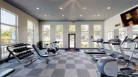 The fitness center at Ashton Brook in Louisville, Kentucky is a thoughtfully designed, single-floor facility built to support a well-rounded workout routine. The space features soaring ceilings accented with a bold teal-painted upper border, recessed lighting, and expansive floor-to-ceiling windows that flood the interior with natural light and provide views of the surrounding greenery and pool area. The checkerboard-patterned carpet tile flooring adds a clean, modern aesthetic throughout.

The cardio zone is well-stocked with multiple treadmills, elliptical machines, and stationary spinning bikes, complemented by a wall-mounted flat-screen television for entertainment during workouts. A full cable machine and multi-function strength station anchor the strength training area, supported by a tiered dumbbell rack with a full range of free weights and adjustable benches for versatile training. Stability balls and additional accessories round out the functional fitness offerings.

Large mirrors line key sections of the walls, visually expanding the space and aiding in form correction. Multiple glass doors provide direct outdoor access, enhancing ventilation and connectivity to the exterior grounds. The overall ambiance is bright, open, and motivating, making it a convenient and comprehensive amenity for residents of Ashton Brook.