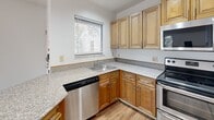 Located at 1500 E Kilgore Rd in Portage, Michigan, this single-floor unit offers an efficient and well-organized layout. The combined kitchen and living room serves as the heart of the space, featuring warm hardwood-style flooring that flows throughout. The living area is bathed in natural light from multiple windows fitted with blinds, and a ceiling fan provides comfortable air circulation. A textured ceiling adds subtle architectural detail to the main living space.

The kitchen is thoughtfully designed with warm-toned wooden cabinetry, granite-style countertops, and a peninsula that provides additional prep space and a casual dining option. Stainless steel appliances — including a refrigerator, range, microwave, and dishwasher — complete the functional kitchen setup. Recessed lighting illuminates the area efficiently.

The two bathrooms offer distinct configurations: one features a tiled shower and tub combination, while the other includes a wooden vanity with a granite-style countertop and a framed mirror. Both maintain a clean, neutral aesthetic with tile flooring. Two closets provide practical storage throughout the unit. Natural light from outdoor greenery filters through the windows, creating a bright and inviting atmosphere across every room.