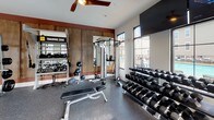 Located at 106 Pullman Ln in Mooresville, NC, this well-equipped fitness center offers a comprehensive workout environment designed to accommodate a wide range of exercise routines. The single-floor facility is bathed in natural light streaming through a series of large, black-framed windows that line the walls, creating an open and energizing atmosphere. Durable speckled rubber flooring spans the entire space, providing both safety and resilience underfoot. Overhead, sleek ceiling fans maintain air circulation throughout the room.

The cardio section is lined with a row of commercial-grade treadmills, ellipticals, and upright bikes — all from True Fitness — positioned along the windowed wall, with a mounted flat-screen TV nearby for entertainment during workouts. The strength and free weight area features a fully stocked dumbbell rack, adjustable benches, cable machines, and a power rack loaded with weight plates, complemented by floor-to-ceiling mirrors that amplify the sense of space. A dedicated Training Zone is marked along one wall, equipped with battle ropes, medicine balls, and suspension training gear. Warm wood-paneled accent walls add a modern, stylish contrast to the crisp white walls and dark architectural trim, giving the fitness center a polished, contemporary aesthetic.