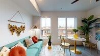 Located at 105 N Killingsworth St in Portland, Oregon, this thoughtfully designed studio unit offers a bright, open-plan layout on a single floor. Large windows flood the living area with natural light and frame views of the surrounding neighborhood, creating an airy and connected atmosphere. The wood-look plank flooring runs throughout, lending warmth and visual continuity to the space.

The kitchen is efficiently designed with light grey cabinetry, white quartz countertops, open shelving, a built-in electric cooktop, a stainless steel sink, a microwave, and a full-size refrigerator — providing all essential functionality in a compact footprint. A ceiling fan overhead enhances comfort in the combined living and sleeping area, which offers generous wall space for personalization and accommodates both a sleeping area and a dining nook.

The bathroom features a walk-in shower with a curtain enclosure, a toilet, and a vanity, all finished in clean, neutral tones. The unit's entry corridor provides a practical transition from the front door into the open living space. Overall, the design balances modern finishes with efficient use of space, making it a functional and inviting urban residence in the Killingsworth neighborhood of North Portland.