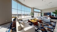 The clubhouse at 880 Pacific Street in Stamford, Connecticut is a thoughtfully designed communal space that blends contemporary architecture with sophisticated, comfortable interiors. Soaring ceilings and sweeping floor-to-ceiling curved windows flood the main lounge with abundant natural light and offer panoramic outdoor views, creating an airy and open atmosphere throughout.

The central lounge serves as the heart of the clubhouse, anchored by a sleek linear fireplace beneath a wall-mounted display screen, flanked by a dramatic accent wall. Bold, geometric patterned area rugs complement plush seating arrangements, while curated artwork adds visual interest. Additional seating nooks feature colorful accent chairs and sofas positioned alongside rich hardwood-toned flooring.

A spacious co-working area provides a built-in desk with bar-height seating, open shelving with décor accents, and ample room for productive use. The dining area accommodates a large gathering table with mid-century modern chairs, bathed in light from oversized windows and contemporary globe pendant lighting, with direct access to an outdoor terrace through sliding glass doors.

The well-appointed kitchen features sleek gray cabinetry, dark stone countertops, open wood shelving with wine glass storage, and a built-in oven—ideal for entertaining. Throughout the space, indoor greenery, curated décor, and a cohesive neutral-toned palette create a refined yet welcoming environment.